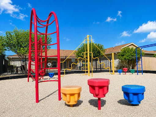 A playground with a red swing set and yellow and blue seesaws.