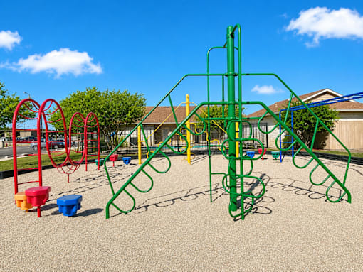 A playground with a green climbing frame and red and yellow swings.