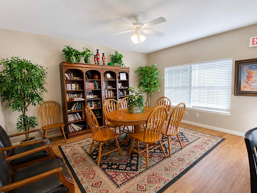 A room with a wooden table and chairs, a bookcase, and a ceiling fan.
