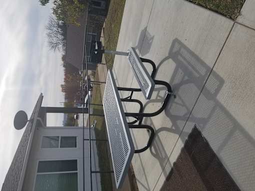 A metal bench with a backrest is on a sidewalk.