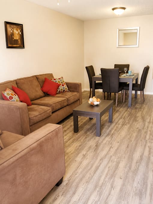 A brown couch with red pillows sits in a living room with a dining table and chairs.
