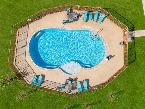 An aerial view of a swimming pool surrounded by a fence and lounge chairs.