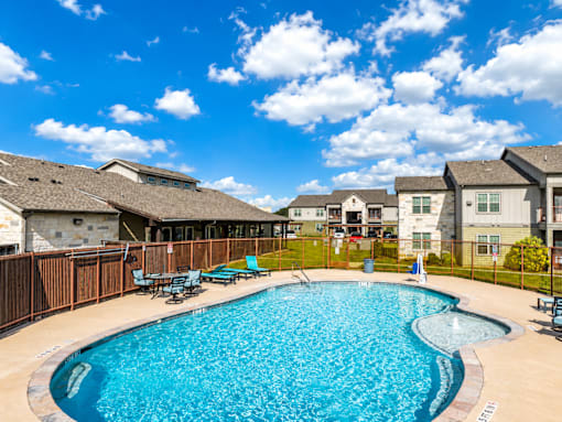 A swimming pool surrounded by a wooden fence and chairs.