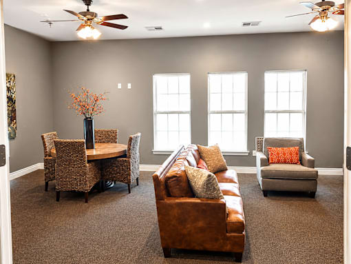 A living room with a brown couch, a table with a vase of flowers, and a ceiling fan.
