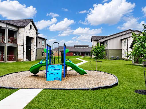 A playground with a green and blue slide in the middle of a grassy area.