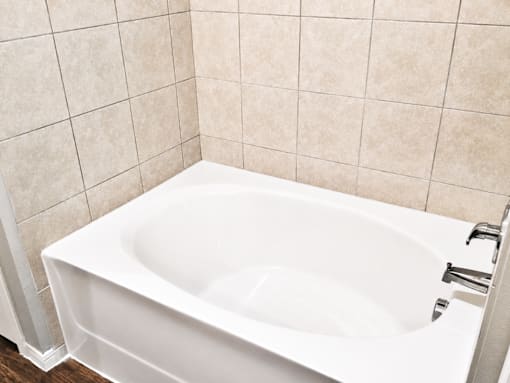 A white bathtub is installed in a bathroom with beige tiles.