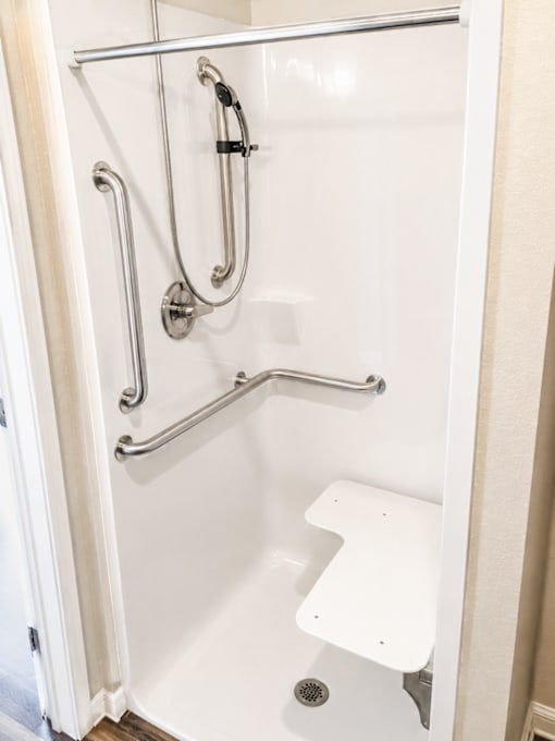 A white shower stall with a white seat and silver grab bars.
