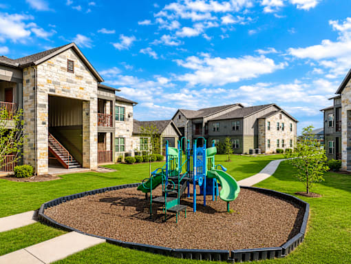 A playground with a green slide and a blue swing set in the middle of a gravel area.