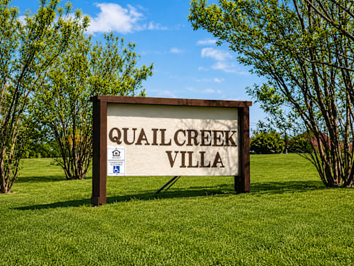 A sign that says Quail Creek Villa stands in a grassy field.
