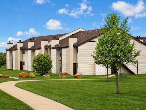 A tree stands in front of a building with a walkway in front of it.