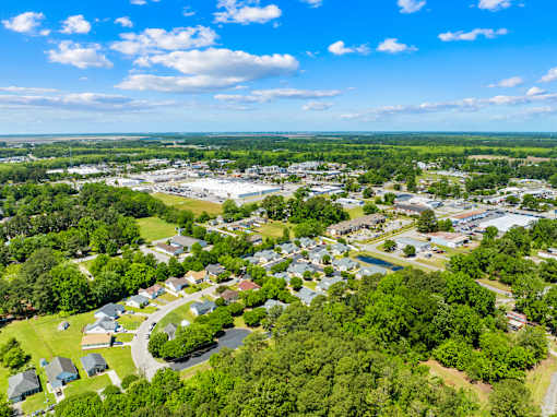 A bird's eye view of a residential area with houses, trees, and a parking lot.