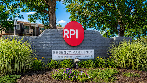 A sign for Regency Park Indy apartments is displayed in front of a building.