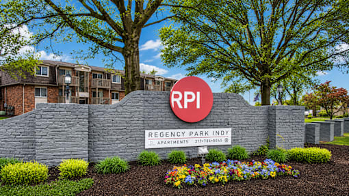 A sign for Regency Park Apartments is in front of a building and trees.