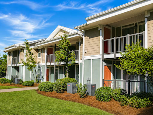 A row of townhouses with green lawns and bushes in front.
