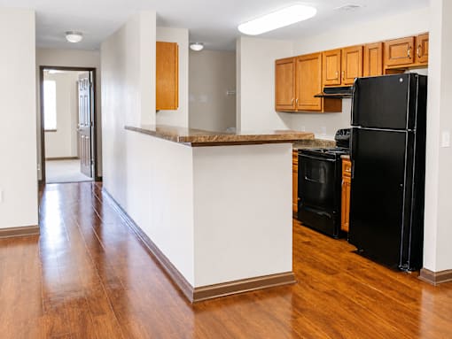A kitchen with a black refrigerator and wooden cabinets.