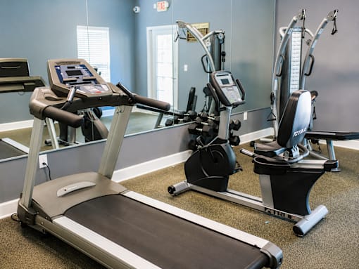 A treadmill and two stationary bikes are in a gym.