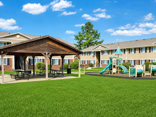 A playground with a green slide and picnic tables in front of a building.