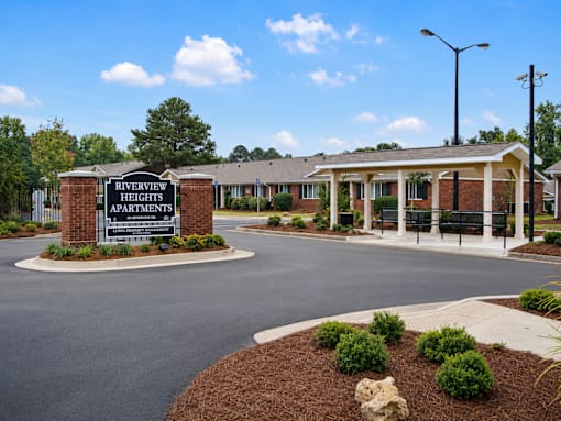 A sign for Riverview Heights Apartments stands in front of a building.