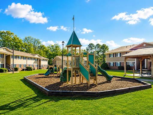 A playground with a green slide and a wooden structure with a flag on top.