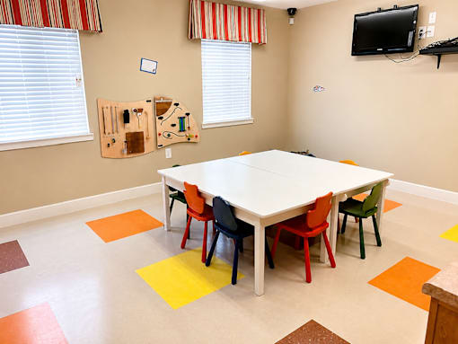A white table surrounded by colorful chairs in a room with a television on the wall.