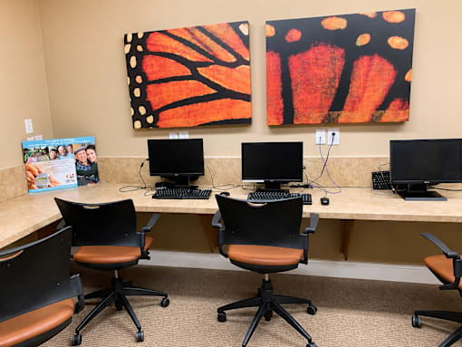 A room with a desk and chairs and two paintings on the wall.