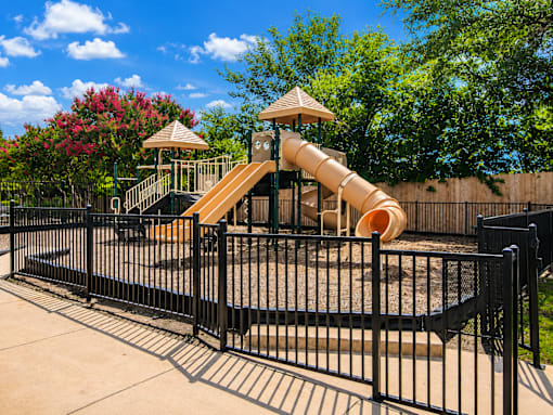 A playground with a yellow slide and a black fence.