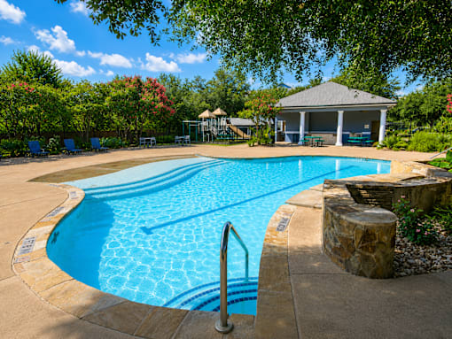 A large swimming pool surrounded by trees and a gazebo.