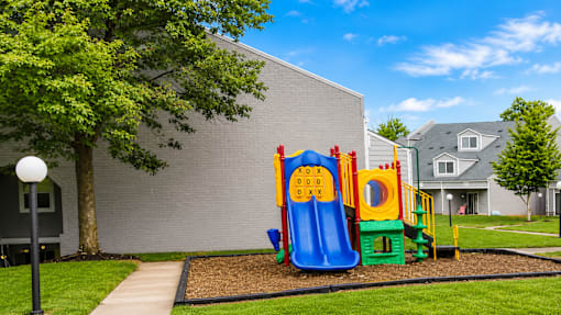 A playground with a slide and a climbing frame is in front of a grey building.