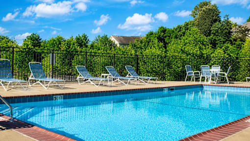 A pool with blue water and white chairs around it.