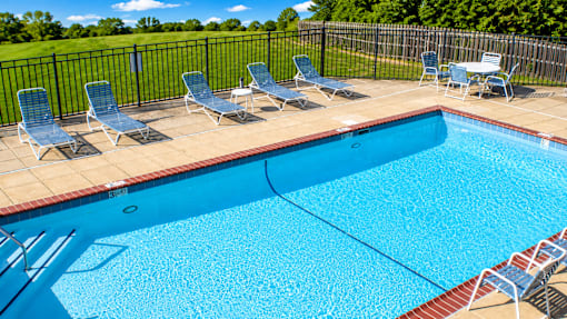 A pool surrounded by chairs and a fence.
