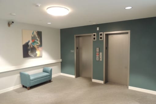 A hallway with a blue chair and a painting on the wall.