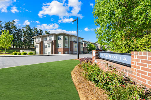 A Magnolia sign is on a brick wall next to a grassy area.