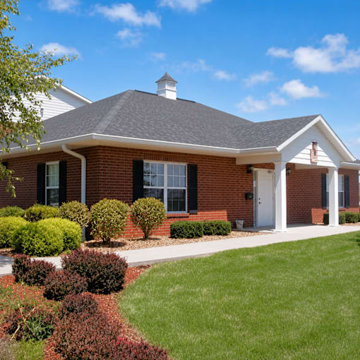 A house with a white door and windows surrounded by bushes.