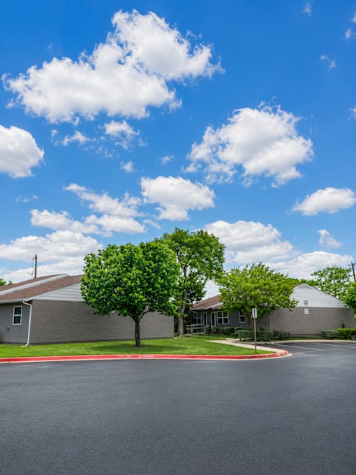 A clear day with a blue sky and fluffy white clouds above a building and a tree.