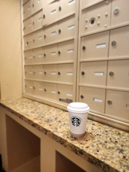 A Starbucks cup sits on a granite countertop in front of a wall of lockers.