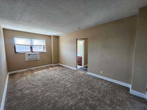 A room with a carpeted floor and a window with blinds.