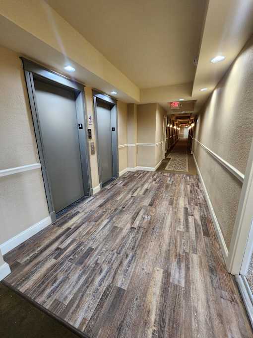 A long hallway with wood floors and two elevators.