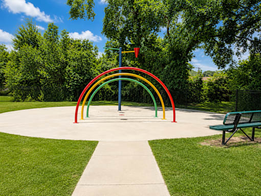 A playground with a rainbow-colored arch and a bench.