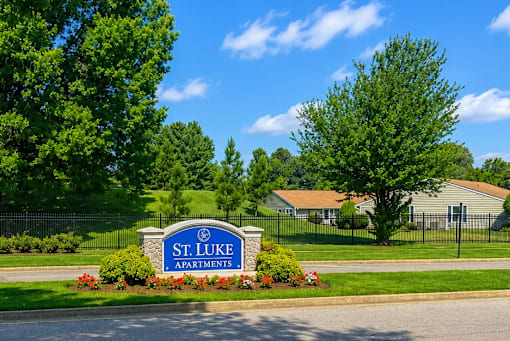 A sign for St. Luke Apartments is in front of a green lawn.