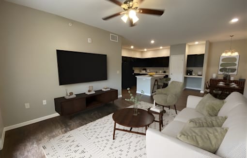 A living room with a white couch, a coffee table, and a flat screen TV mounted on the wall.