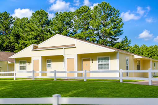 A yellow house with a white fence in front of it.