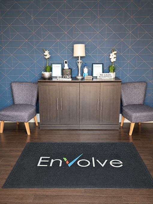 A room with a black carpet that says Envolve and a cabinet with two chairs.