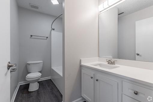 A white toilet in a small bathroom with a white sink and a mirror.