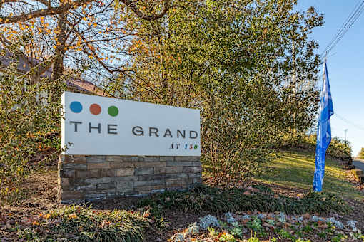 A sign that says "The Grand at 150" is in front of a tree.