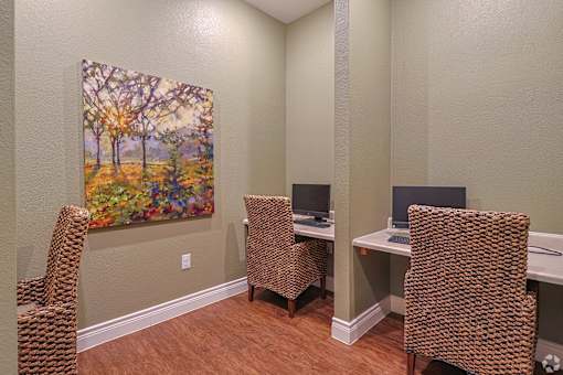 A painting of a tree with autumn leaves hangs on a wall above a desk with two chairs.