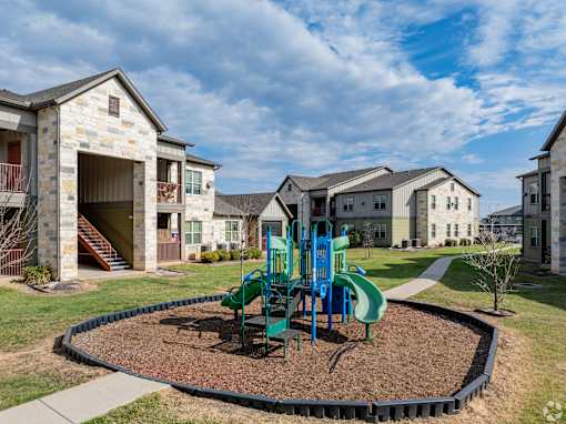 A playground with a green slide and a brown sandbox in the middle of a grassy area.