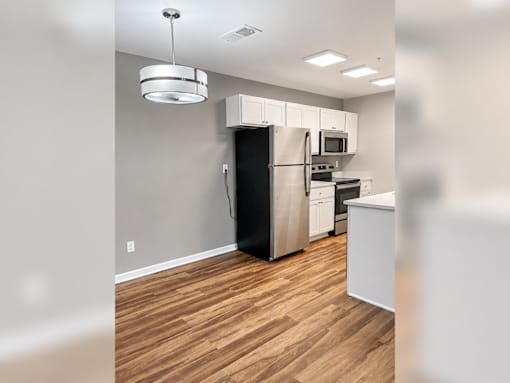 A kitchen with a black refrigerator, white cabinets, and wooden floors.