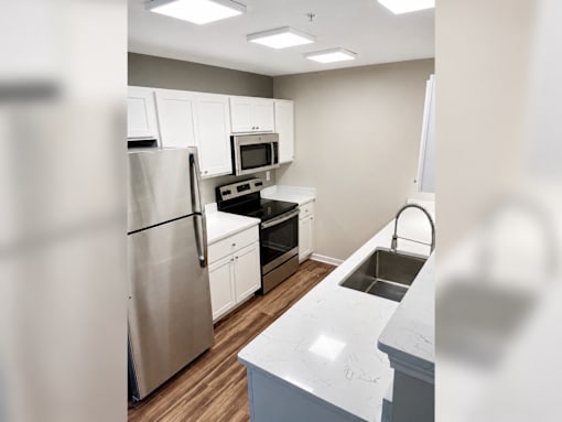 A kitchen with a refrigerator, oven, microwave, sink and cabinets.