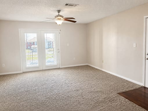 A room with a carpeted floor, a ceiling fan, and a sliding glass door.