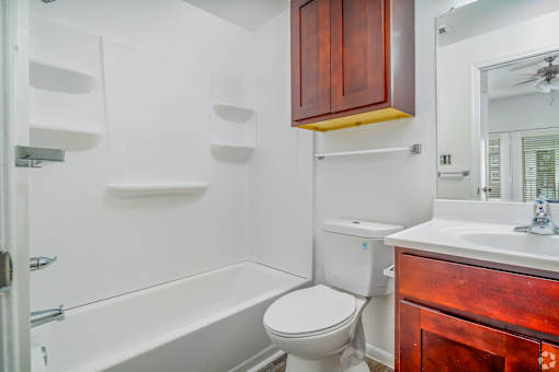 A white toilet sits next to a white bathtub in a bathroom with wooden cabinets.